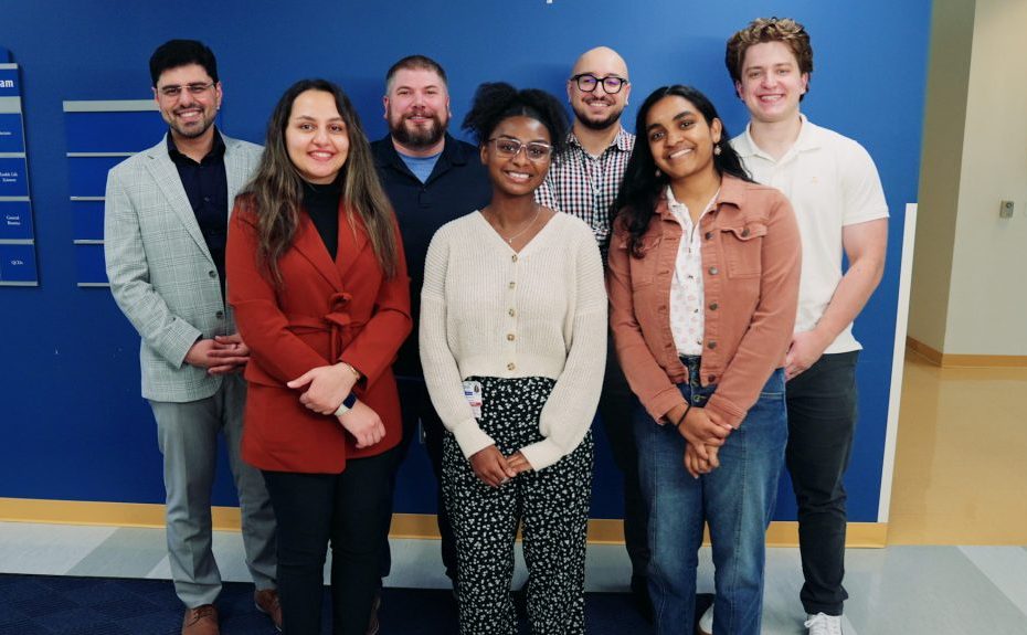 a group of seven researchers smiling in front of a blue wall